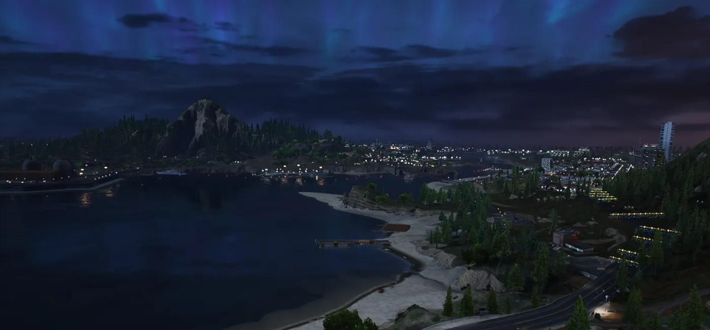 A curving beach and a lit coastal town at night under a sky streaked with blue-green northern lights, with towers on the right and a mountain across the water