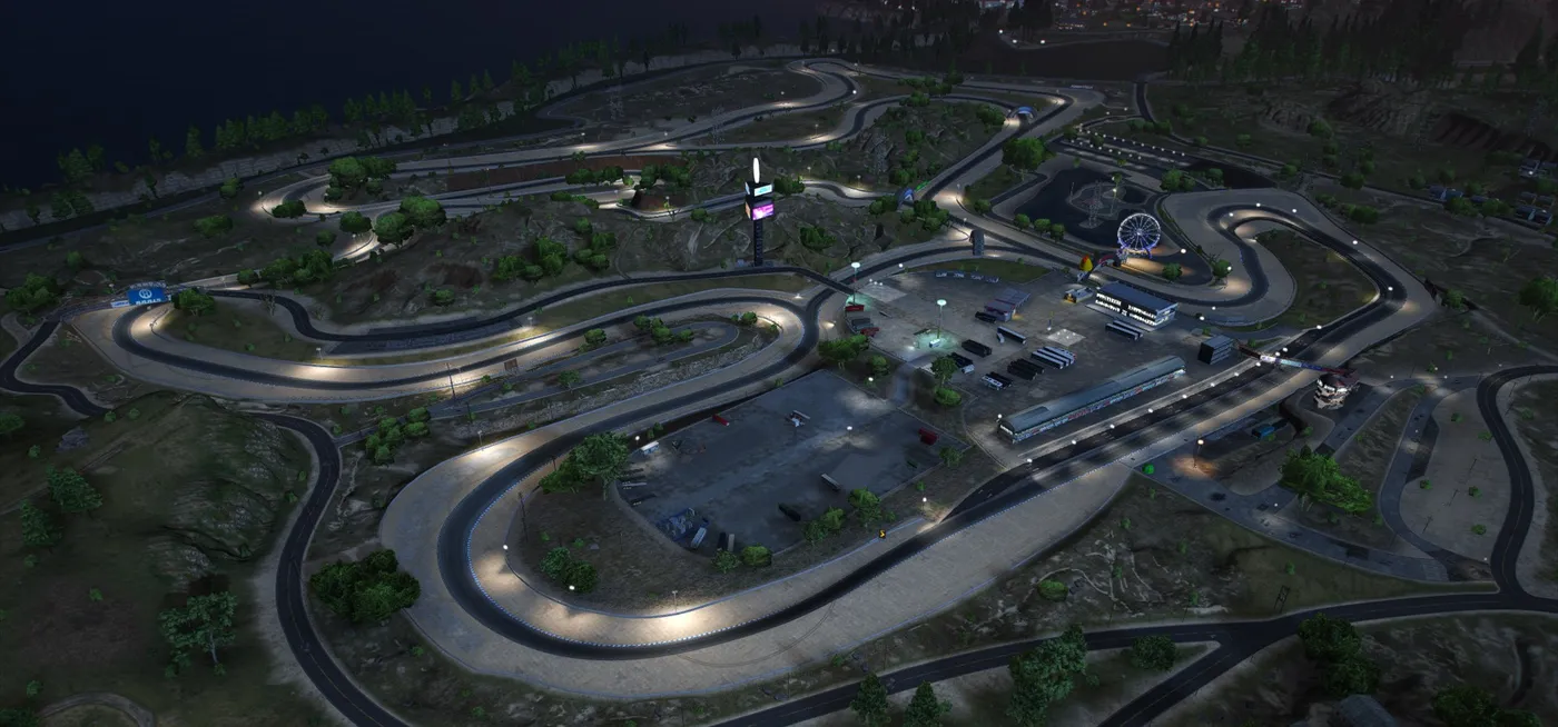 A floodlit race circuit at night winding through scrubby hills, with pit buildings, a tall tower and a Ferris wheel in the infield